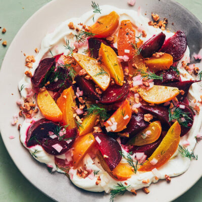 Labneh topped with roasted beets and fresh herbs on a light green table