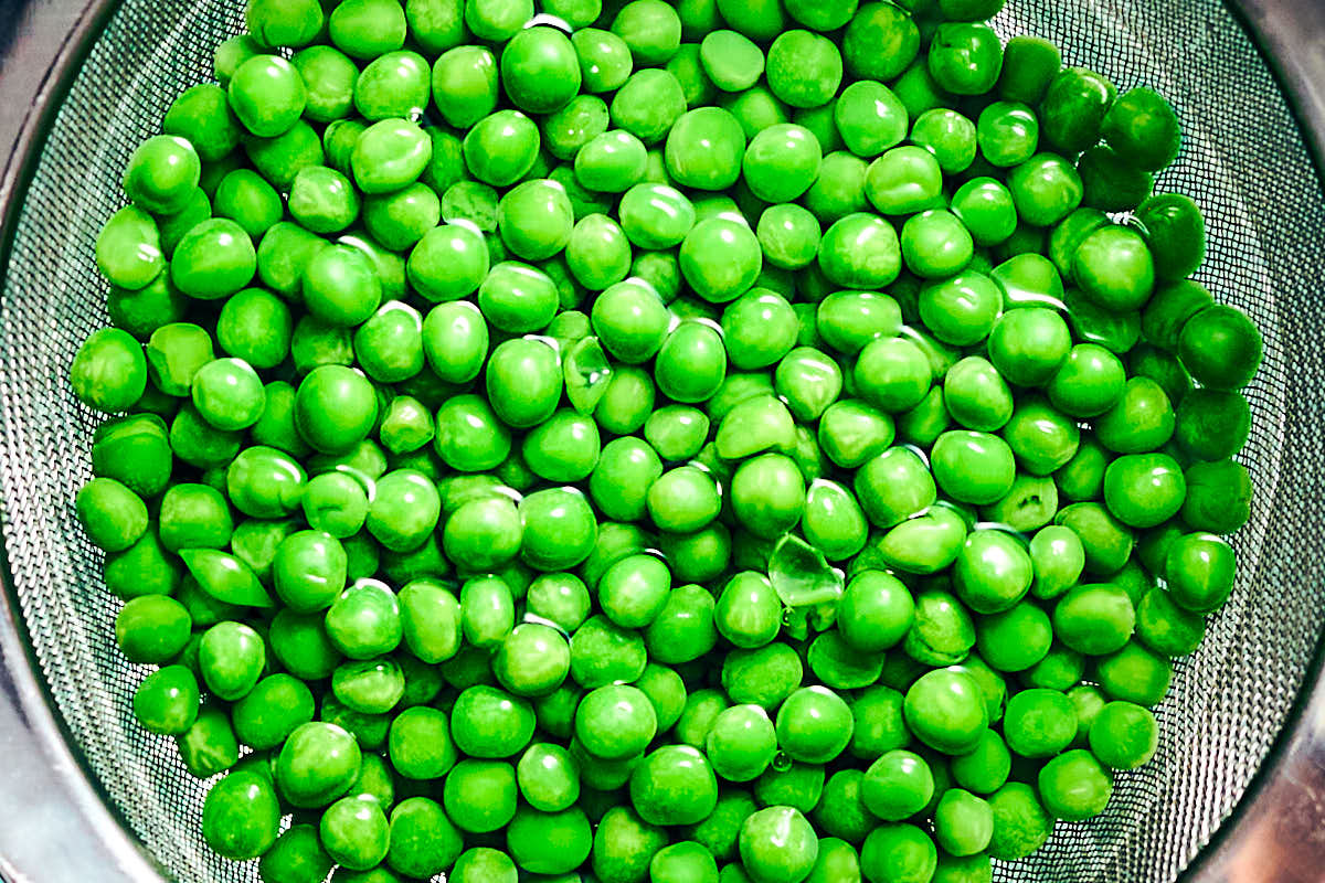 Frozen peas defrosting in hot water in a bowl.