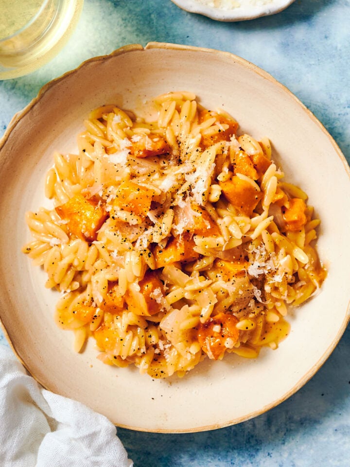 Pumpkin orzo topped with pepper and Parmesan on a plate.