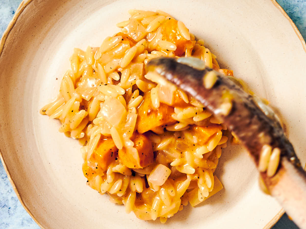 Pumpkin Orzo being spooned onto a dinner plate.