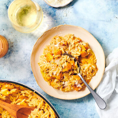 A plate of Peppery Pumpkin Orzo on a dining table with Parmesan and white wine.