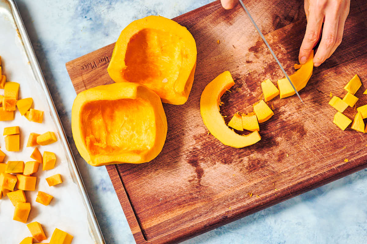 Pumpkin being chopped on a cutting board, then scattered on a baking sheet.