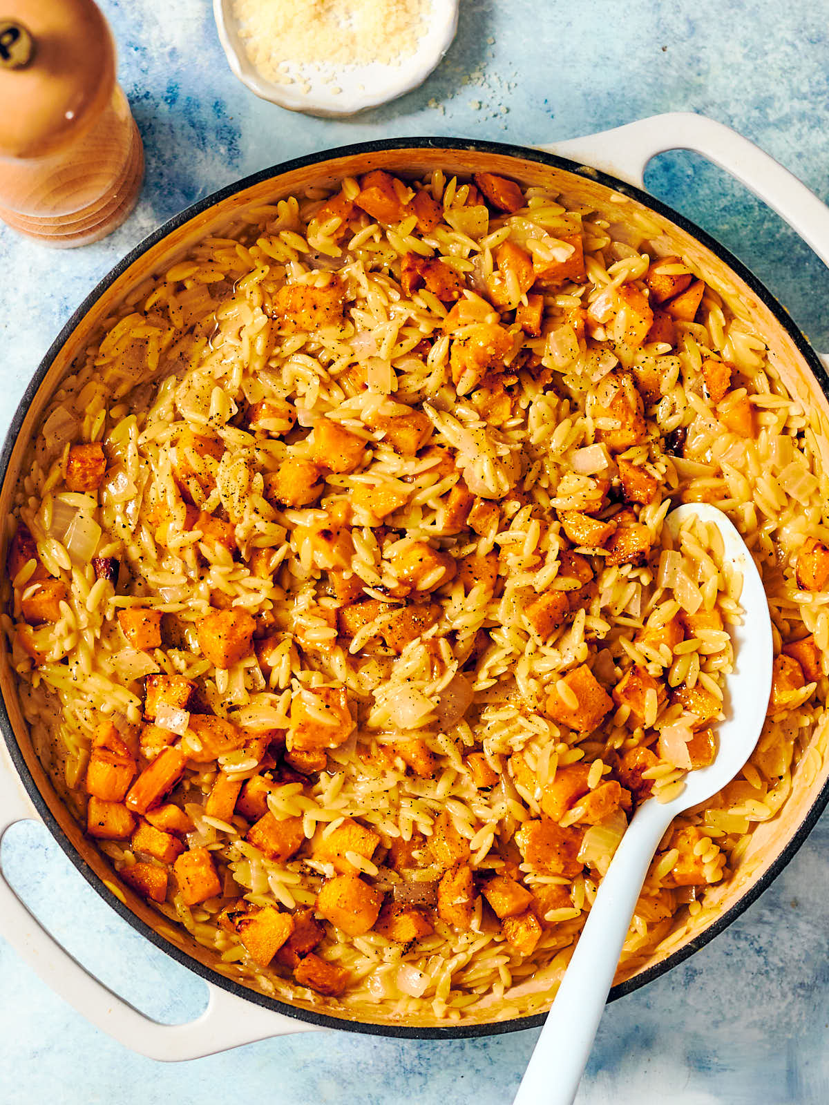 A skillet of vegetarian pumpkin orzo with a serving spoon.