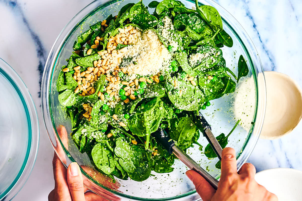 Mixing spinach with pesto salad dressing in a glass bowl.