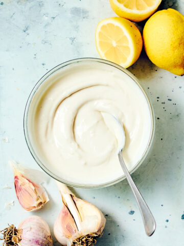 Creamy Shawarma sauce in a bowl with a spoon, with lemons and garlic.