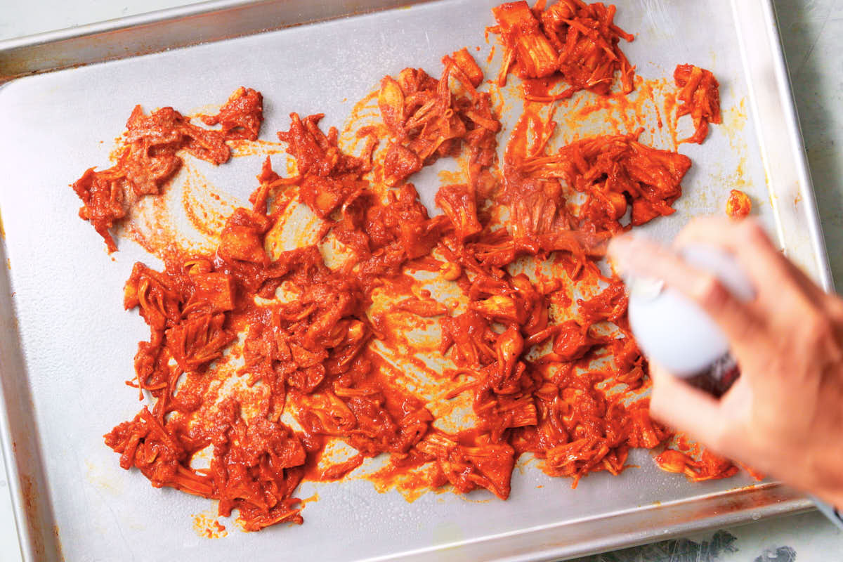 Spreading spiced jackfruit out on a baking sheet to bake for vegan shawarma.