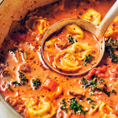 A ladle scooping out Creamy Vegetarian Tortellini Soup out of the pot for serving.
