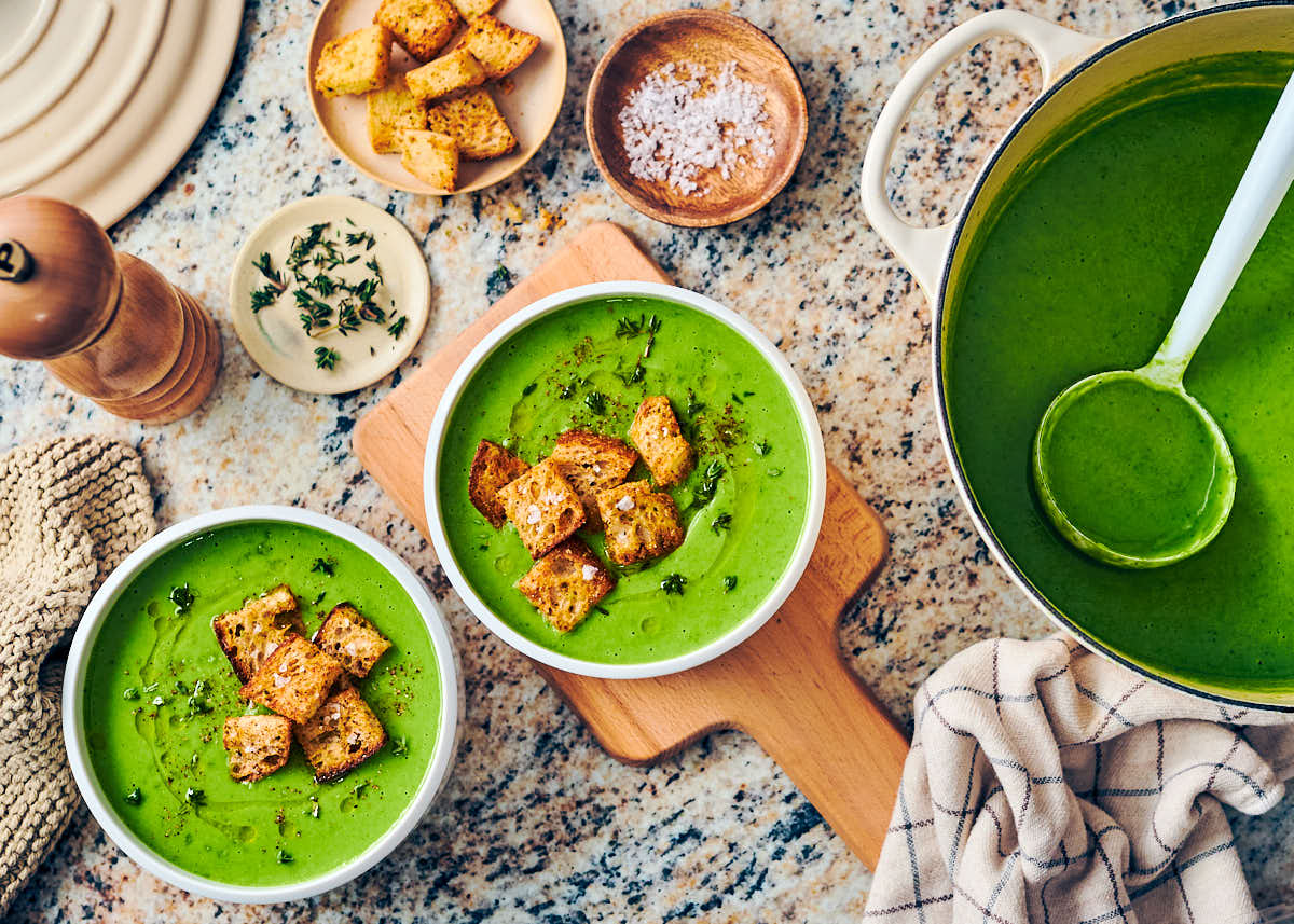 Pea soup in bowls on a table with croutons, thyme, and salt.