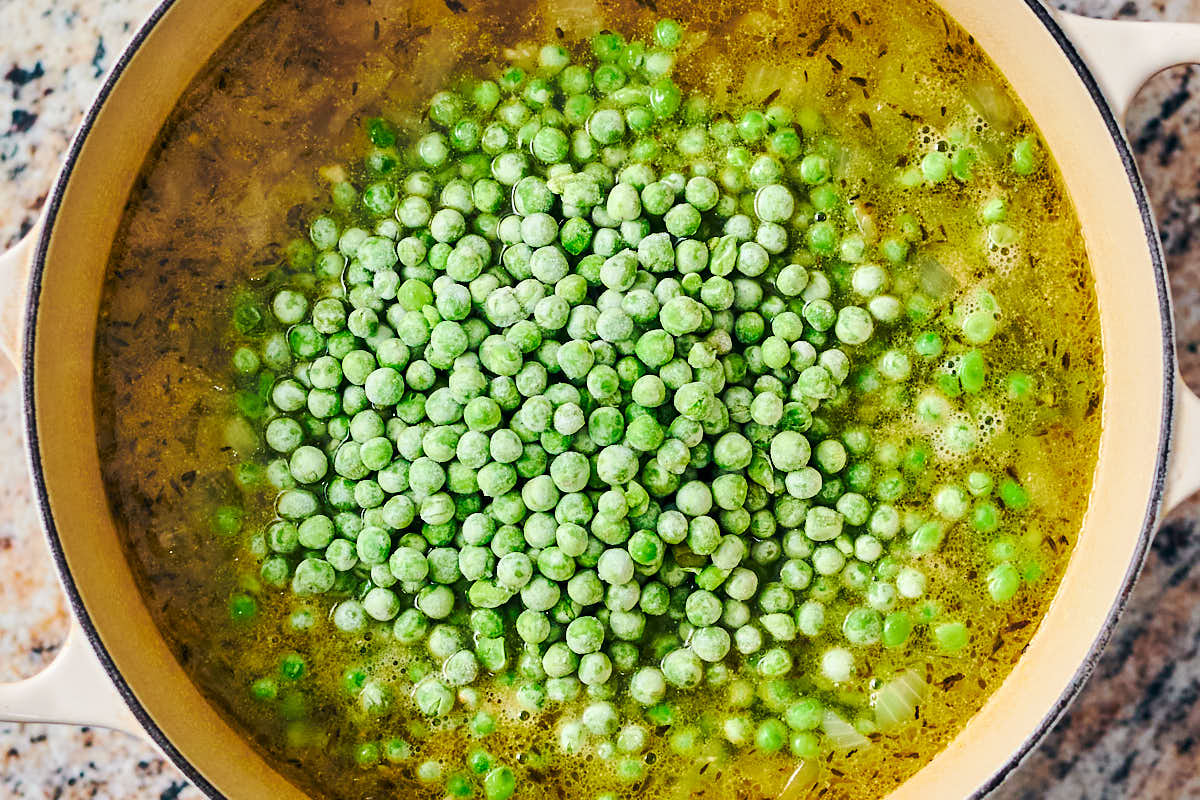 Frozen peas being added to a pot of soup.