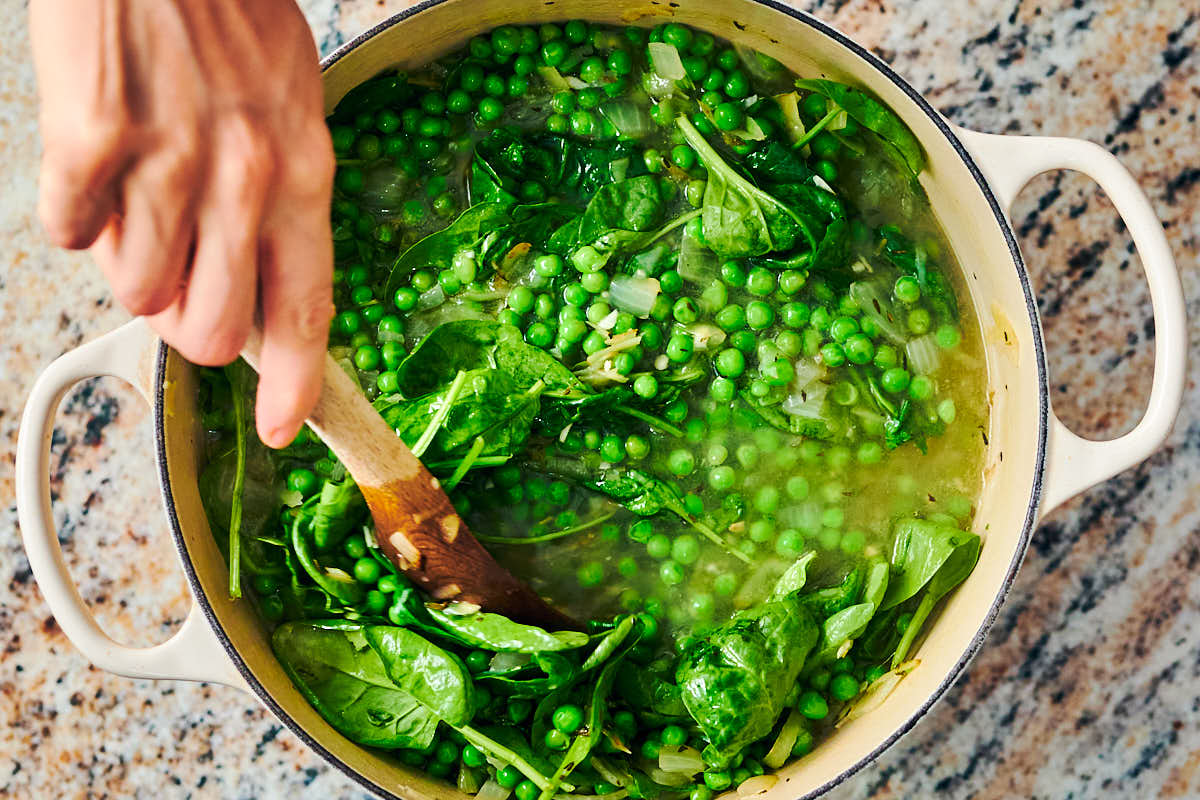 Baby spinach being stirred into a pot of soup made with frozen peas.