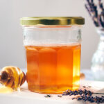 A jar of infused lavender honey with a honey stick and dried lavender.
