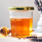 A jar of infused lavender honey with a honey stick and dried lavender.