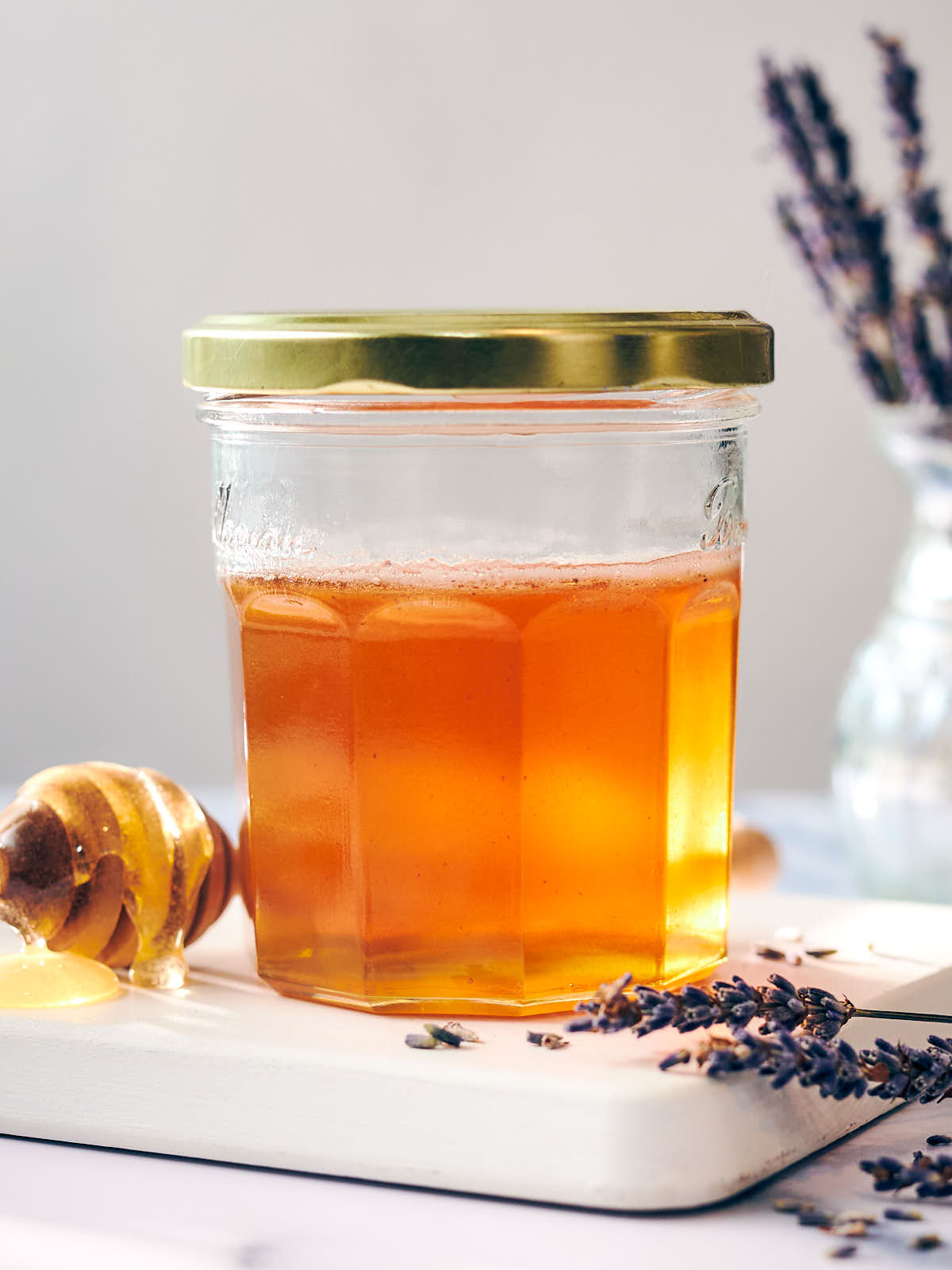 A jar of infused lavender honey with a honey stick and dried lavender blossoms.