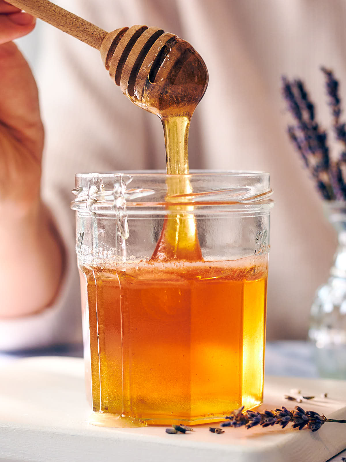 A honey stick being dipped into a jar of infused lavender honey.