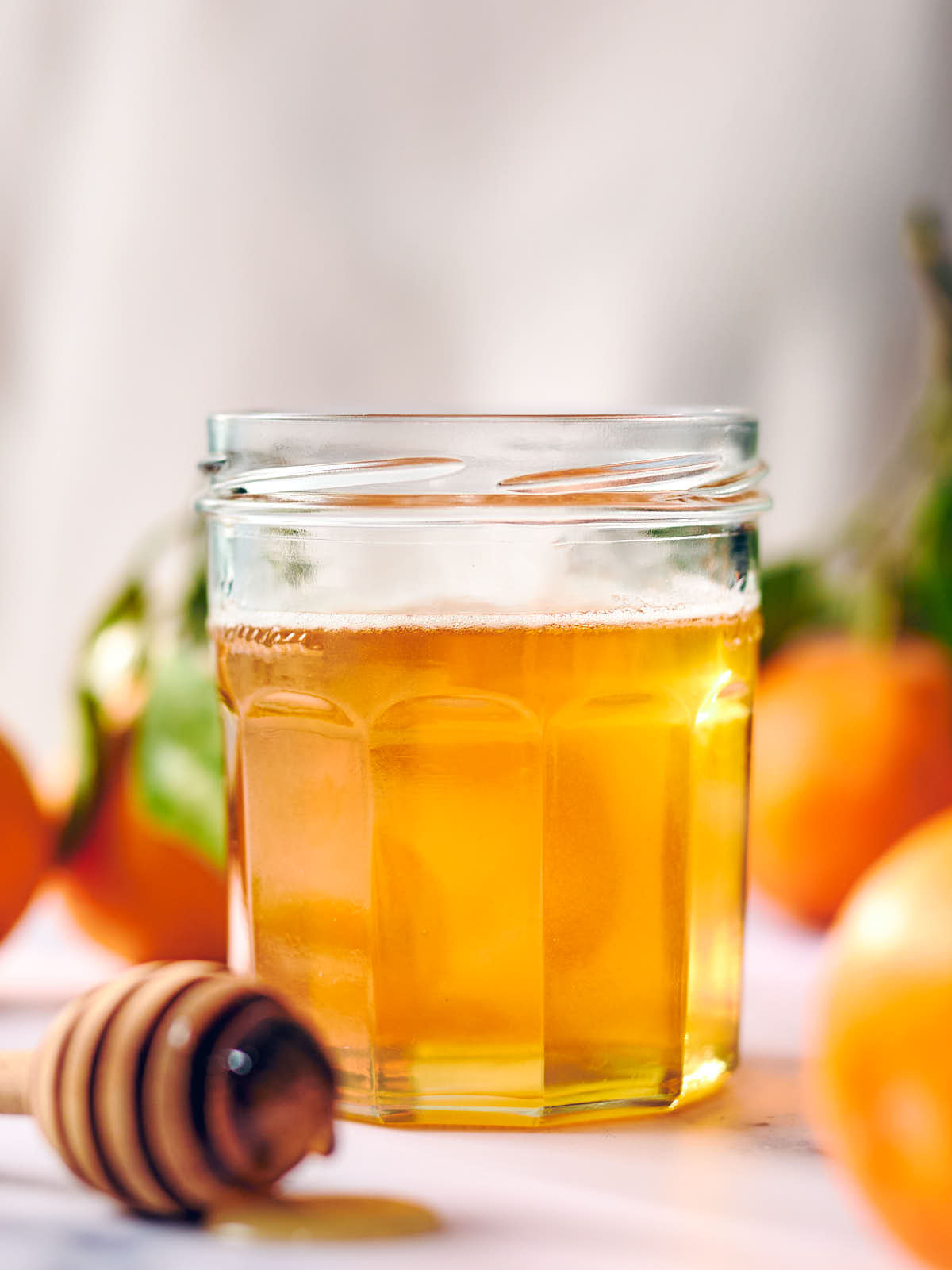 Infused orange honey in a glass jar with a honey spoon. 