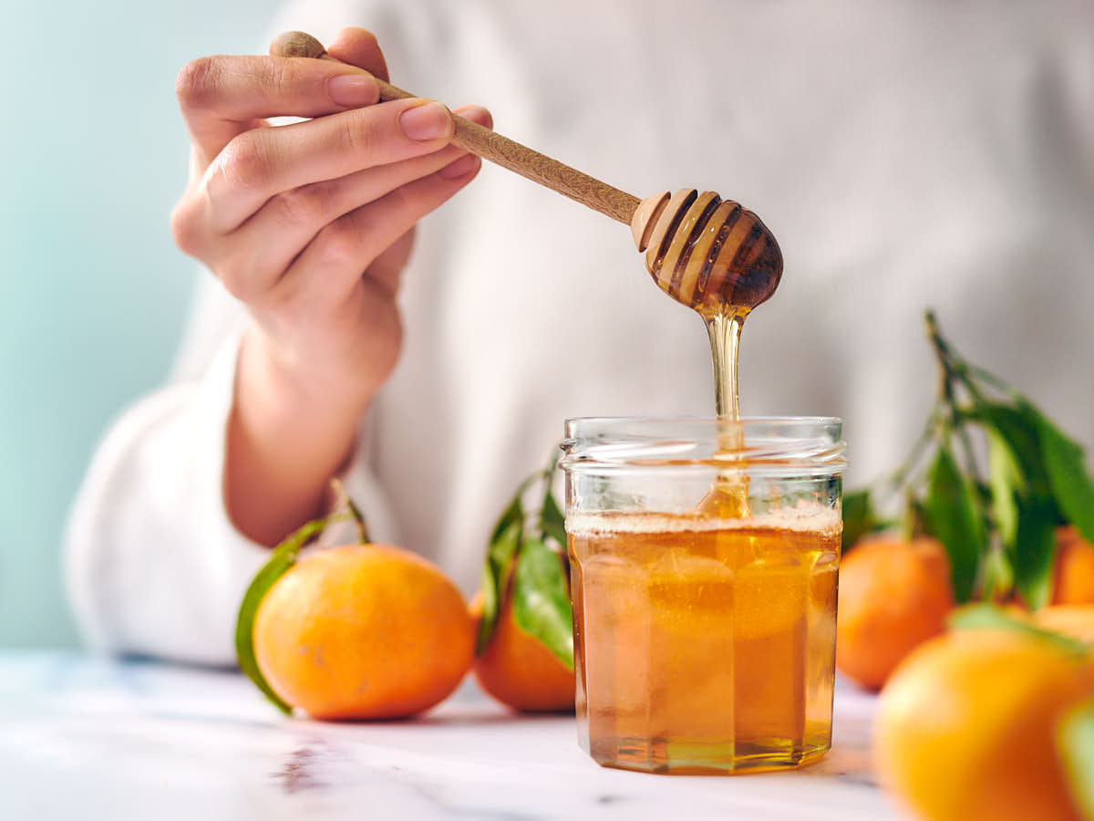 A woman holding a honey stick above a jar of infused orange honey.