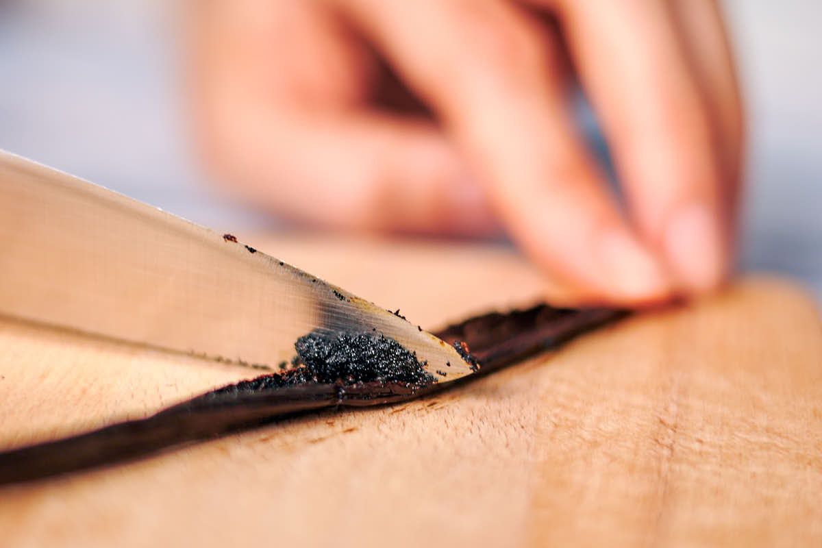 Scraping a vanilla bean on a cutting board with a knife.