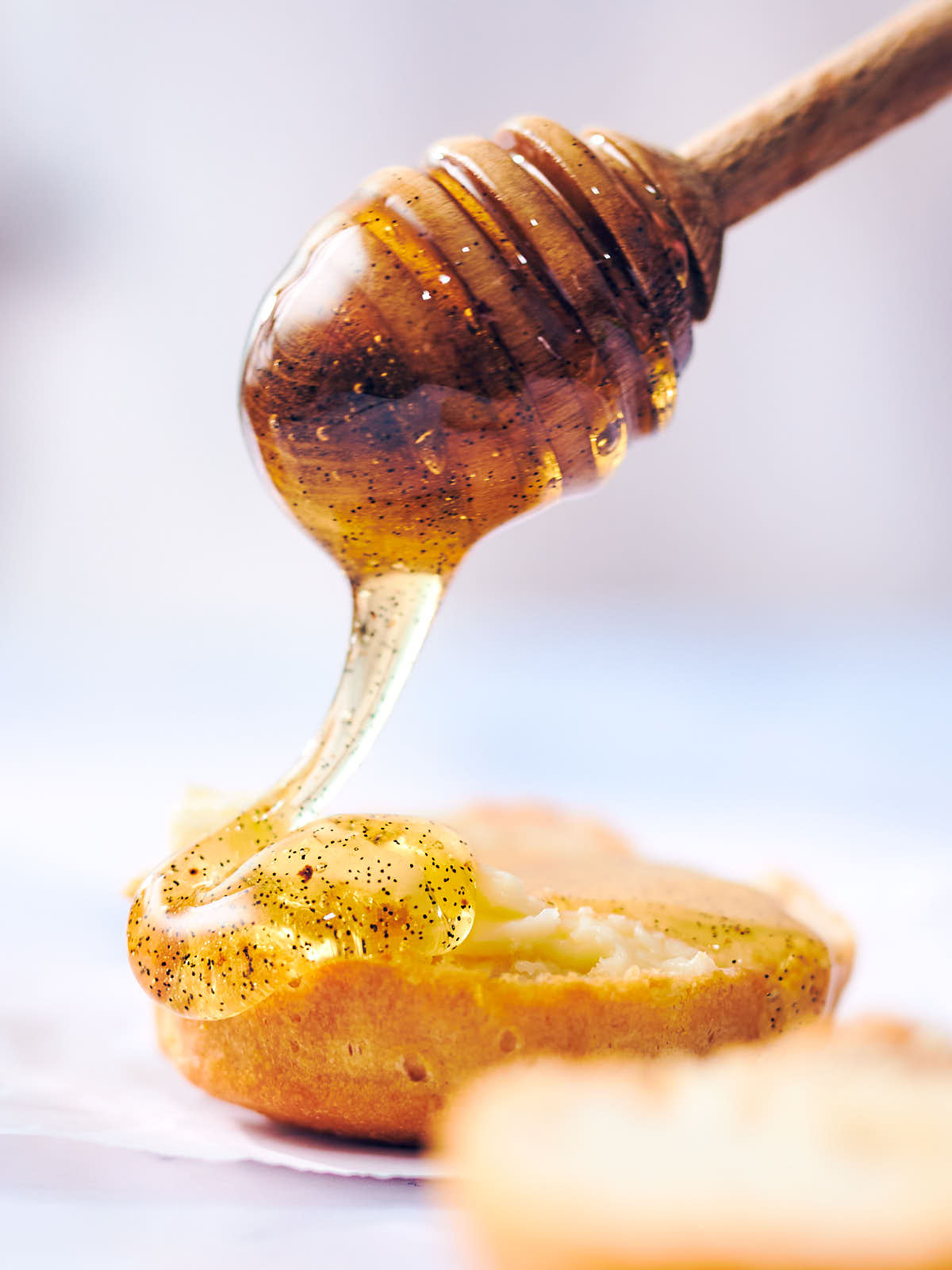 Easy Infused Vanilla Honey being drizzled onto a biscuit with a honey stick.