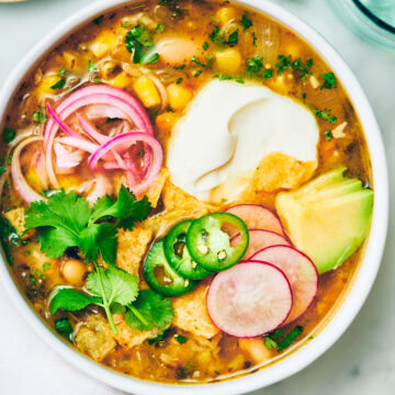 Vegan Green Chili Soup in a bowl with sour cream, pickled onions and cilantro.