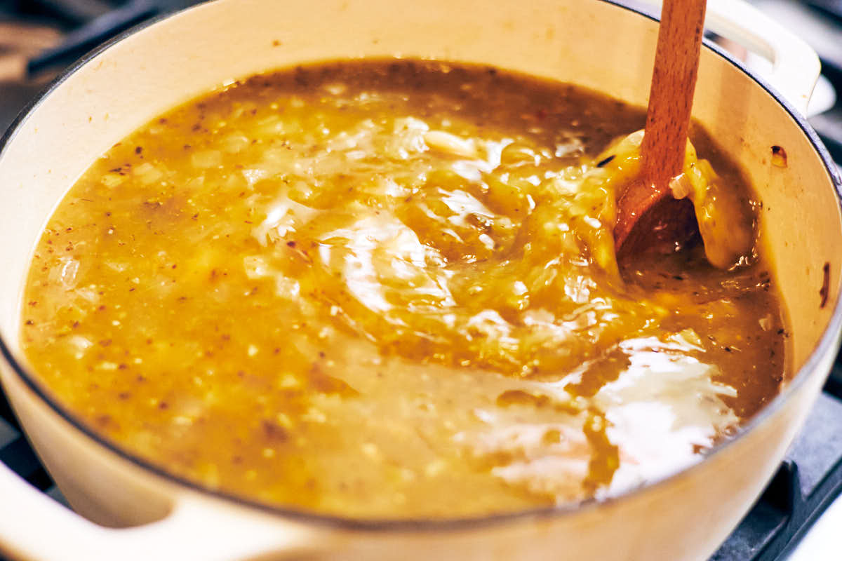 A wooden spoon stirring a pot of soup made with salsa verde and rice.