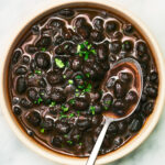 Smoky Stewed Black Beans in a bowl topped with a spoon.