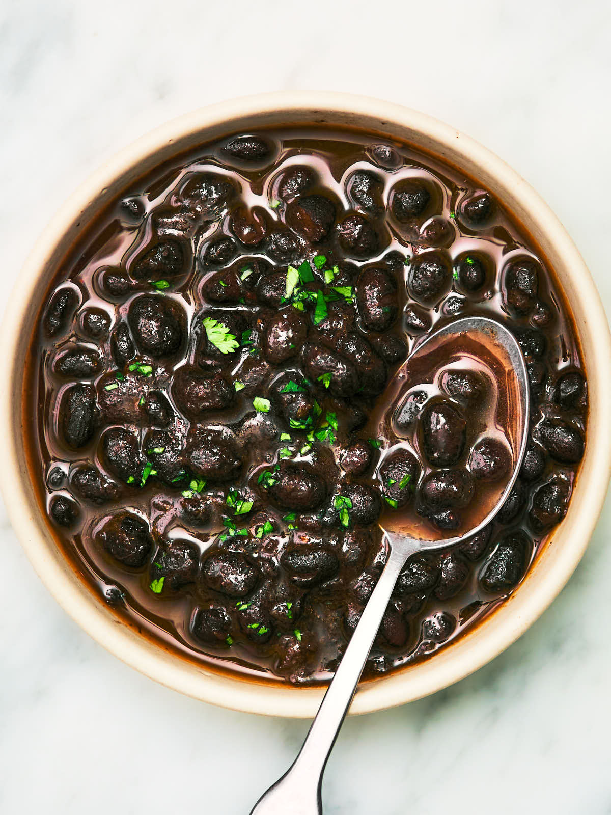 Smoky Stewed Black Beans in a bowl topped with a spoon.