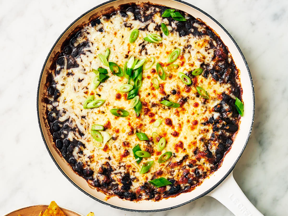 Stewed beans in a skillet topped with cheese and scallions.