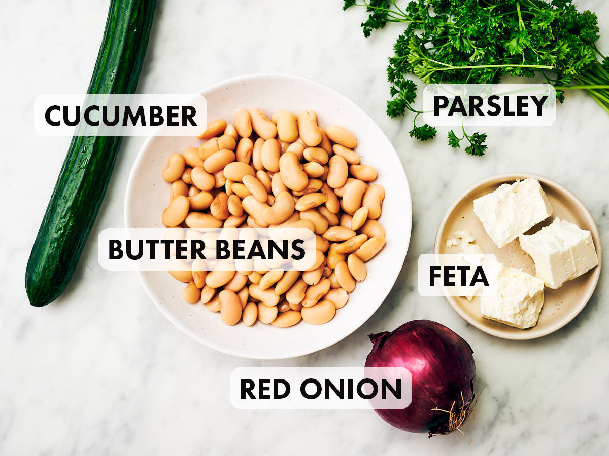 Ingredients to make butter bean salad recipe with cucumber, red onion, parsley, and feta.