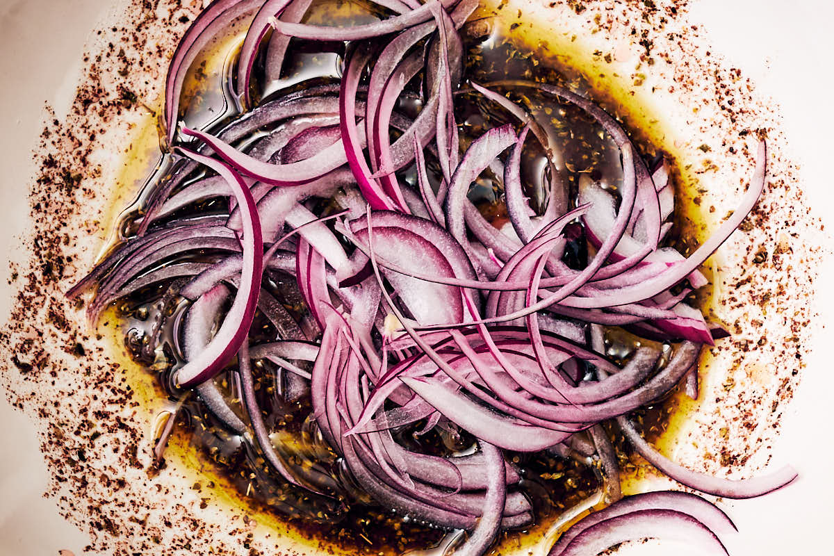 Red onions marinating in a bowl of sumac dressing.