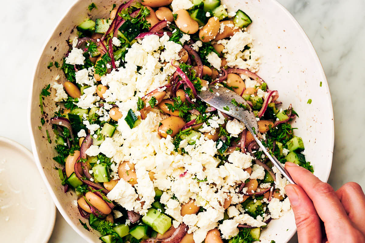 Tossing butter bean salad with feta in a bowl for serving.