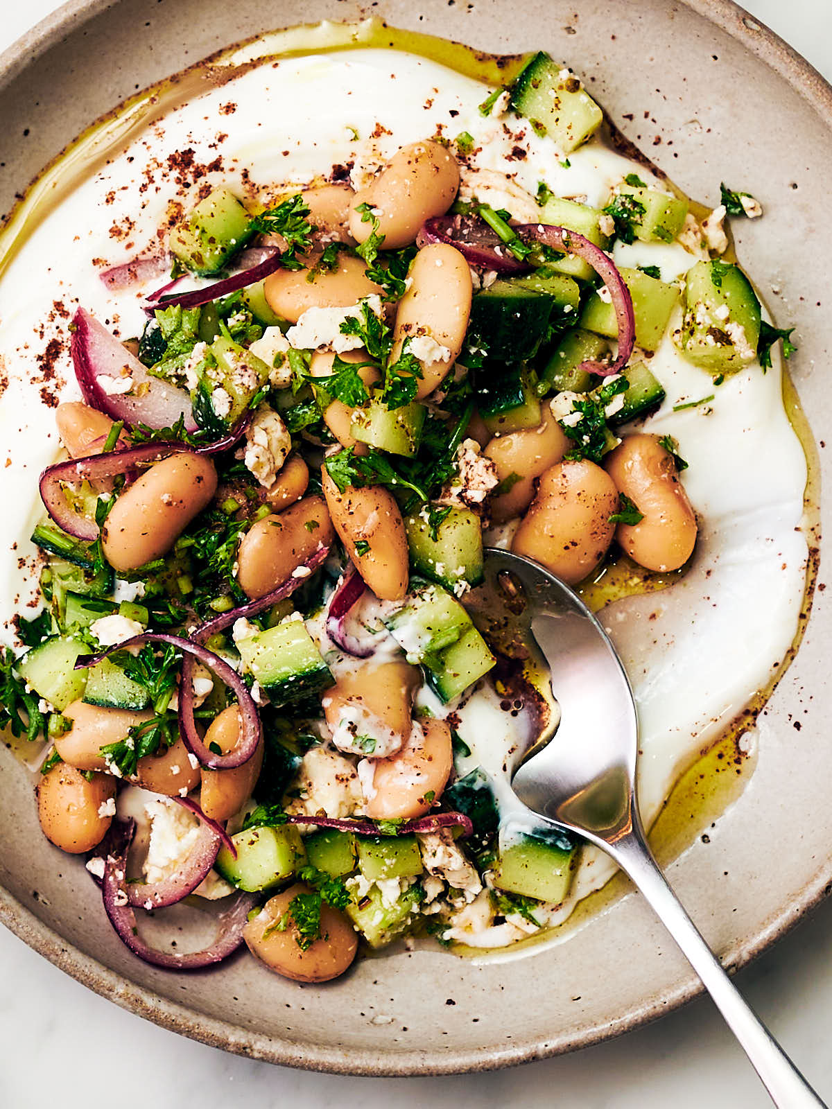 Butter bean salad with feta and cucumber and sumac onions on a plate with a spoon.
