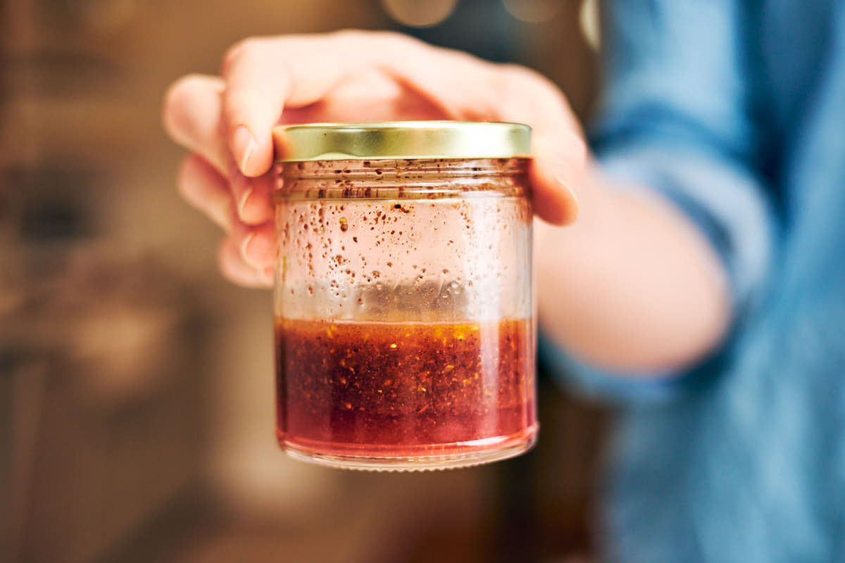 A hand holding a glass jar of sumac vinaigrette.