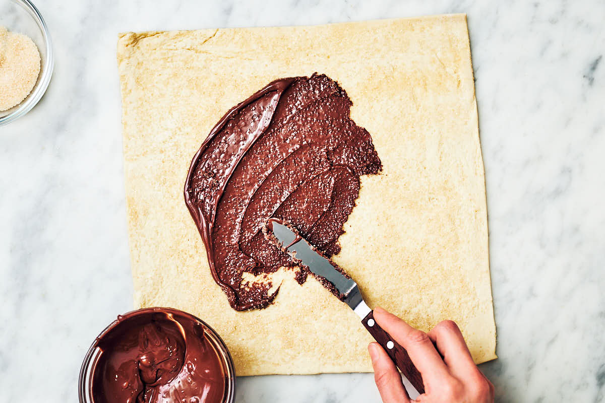 Spreading nutella on top of puff pastry with offset spatula.