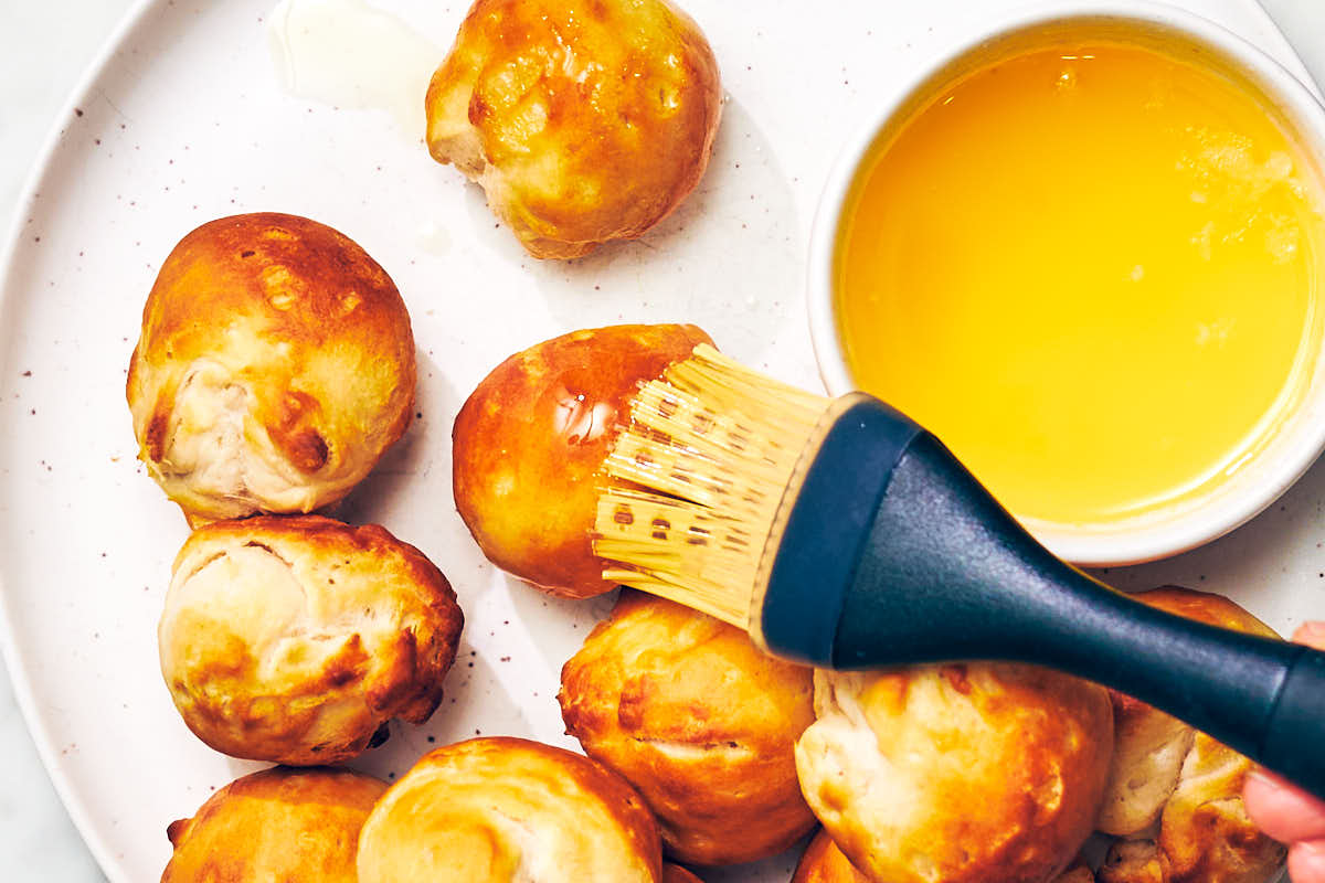 Brushing air fried donut holes with melted butter.