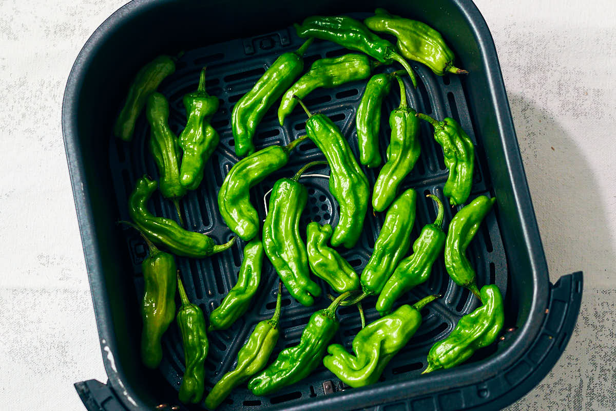 Shishito peppers in an air fryer basket before baking.