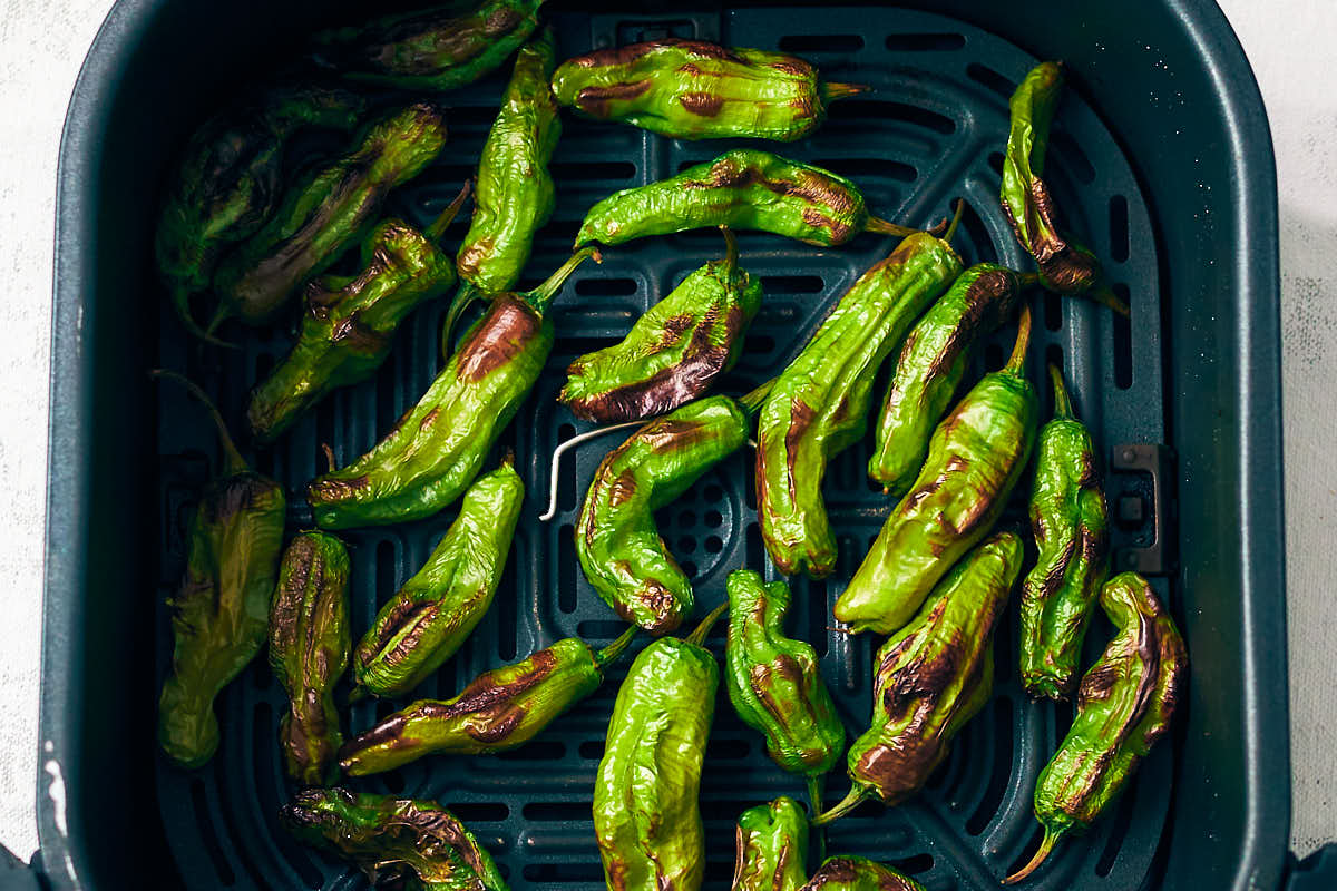 Blistered shishito peppers in an air fryer basket.