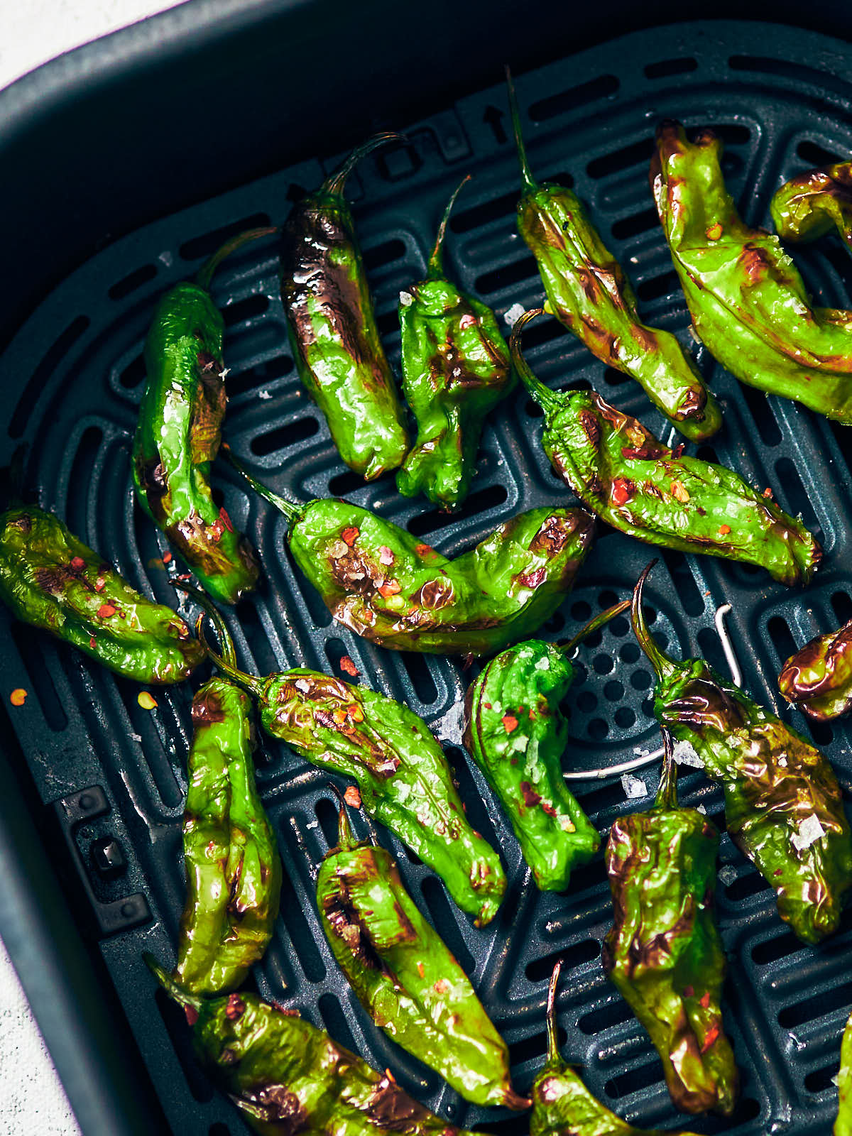 Blistered shishito peppers with lemon and sesame in an air fryer basket.