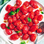 The best roasted air fryer tomatoes on a plate with fresh basil and a serving spoon.