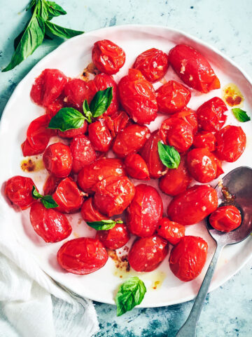 The best roasted air fryer tomatoes on a plate with fresh basil and a serving spoon.