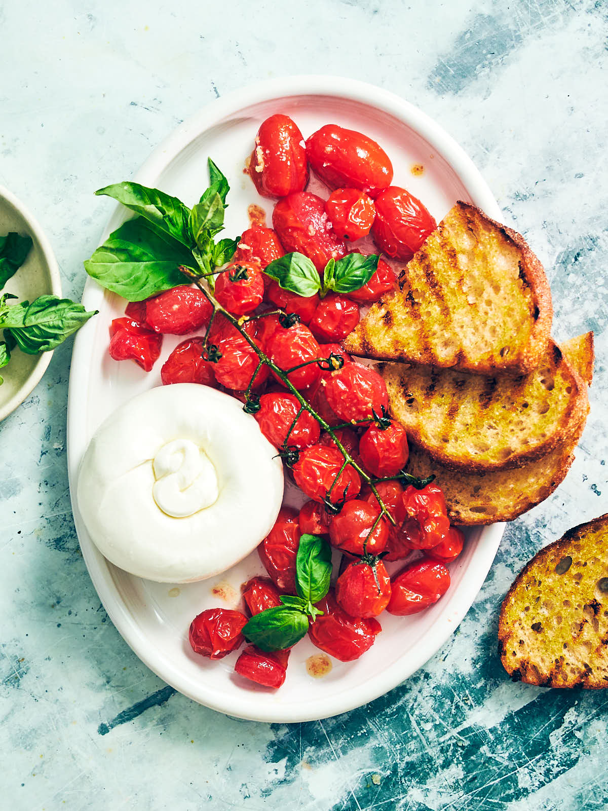Air Fryer Tomatoes on a serving platter with burrata cheese, bread, and fresh basil.