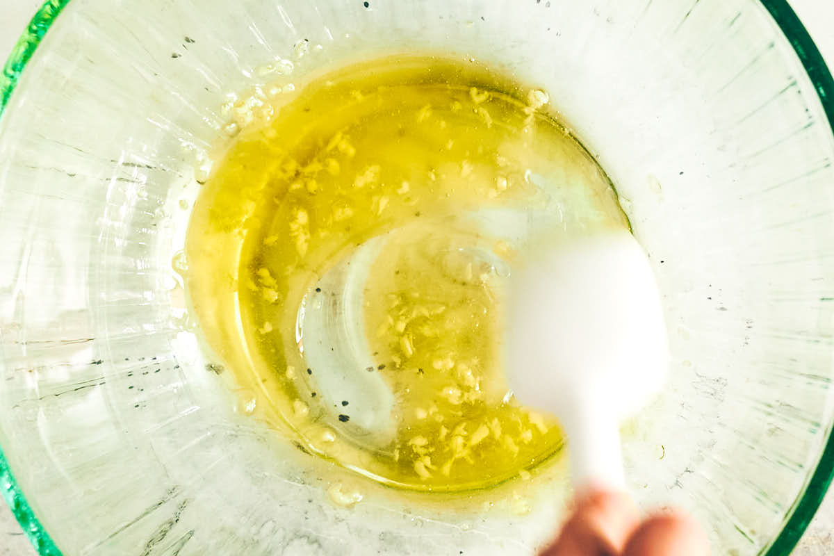 Olive oil and garlic being stirred together in a bowl with a spoon.