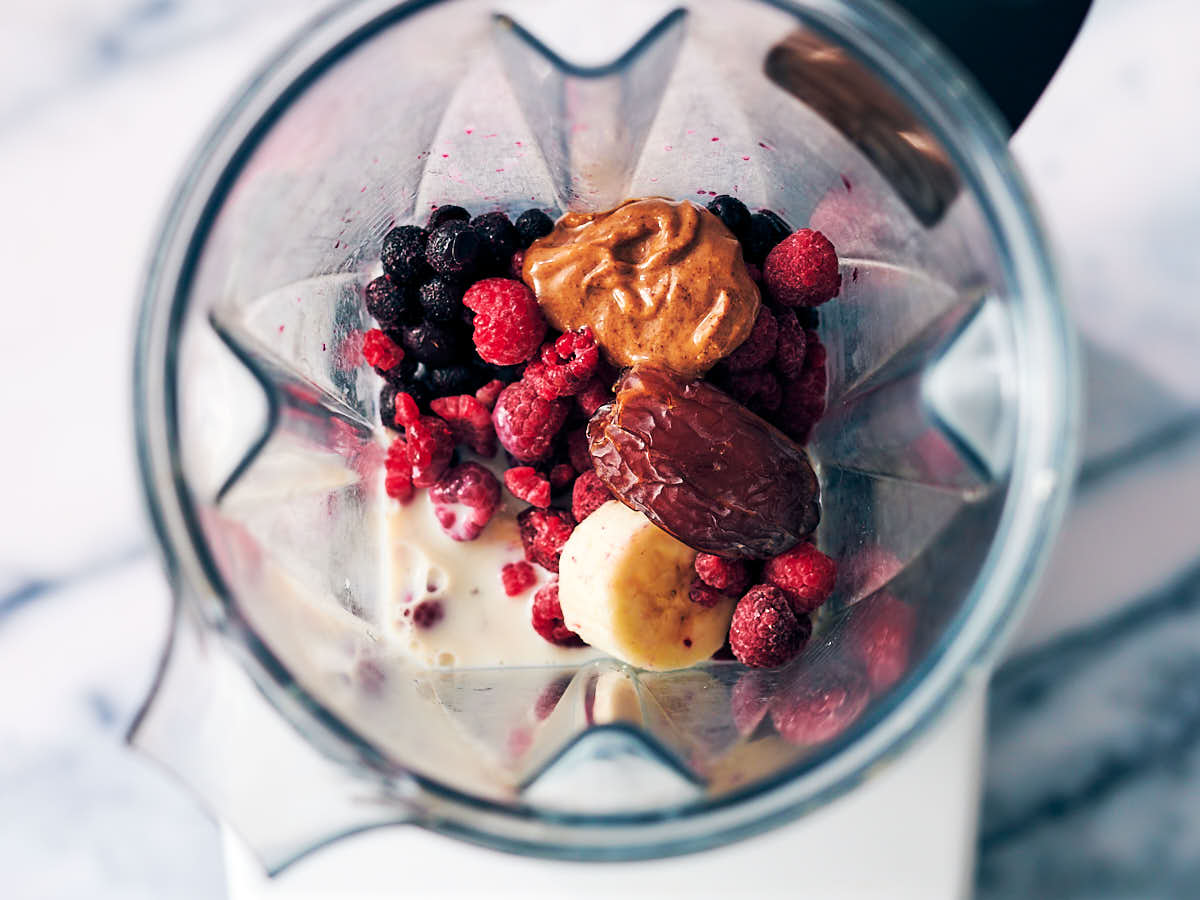 Frozen blueberries, raspberries, banana, date, almond butter and milk in a blender container.