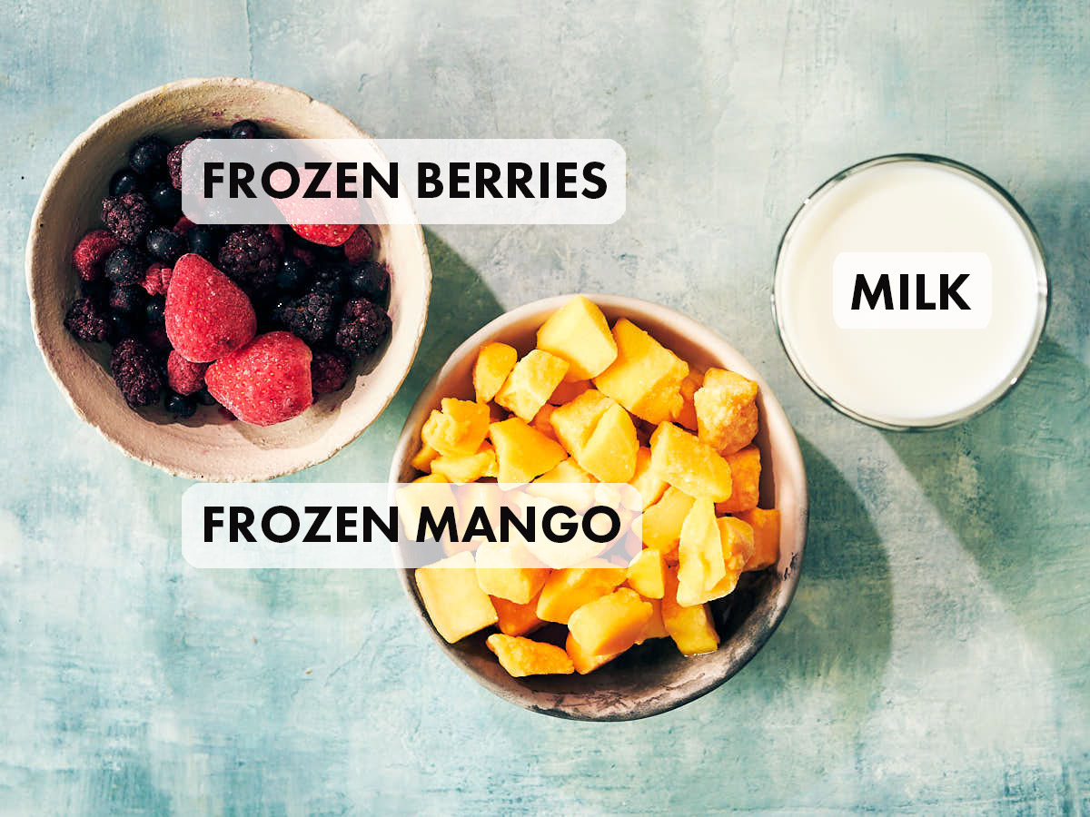 Frozen berries, frozen mango, and milk on a counter.
