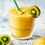 Mango Kiwi Smoothie in a glass topped with fresh kiwi fruit.