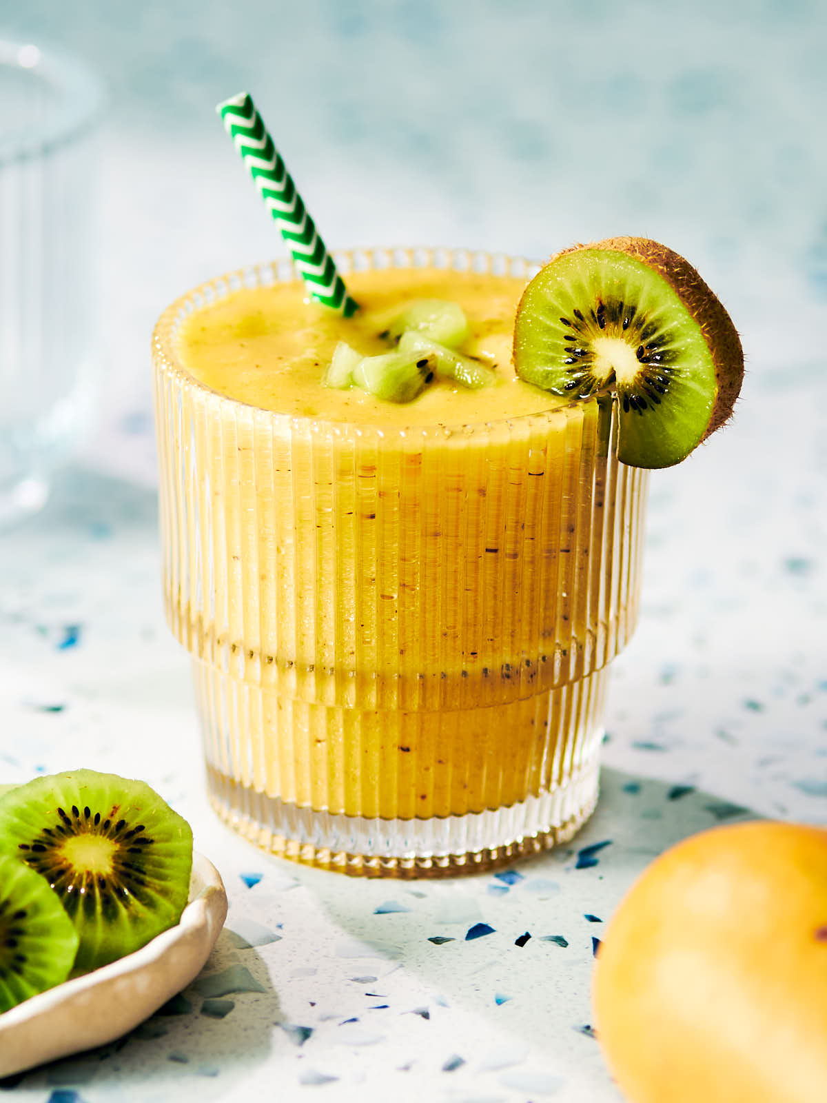 Mango Kiwi Smoothie in a glass topped with fresh kiwi fruit.