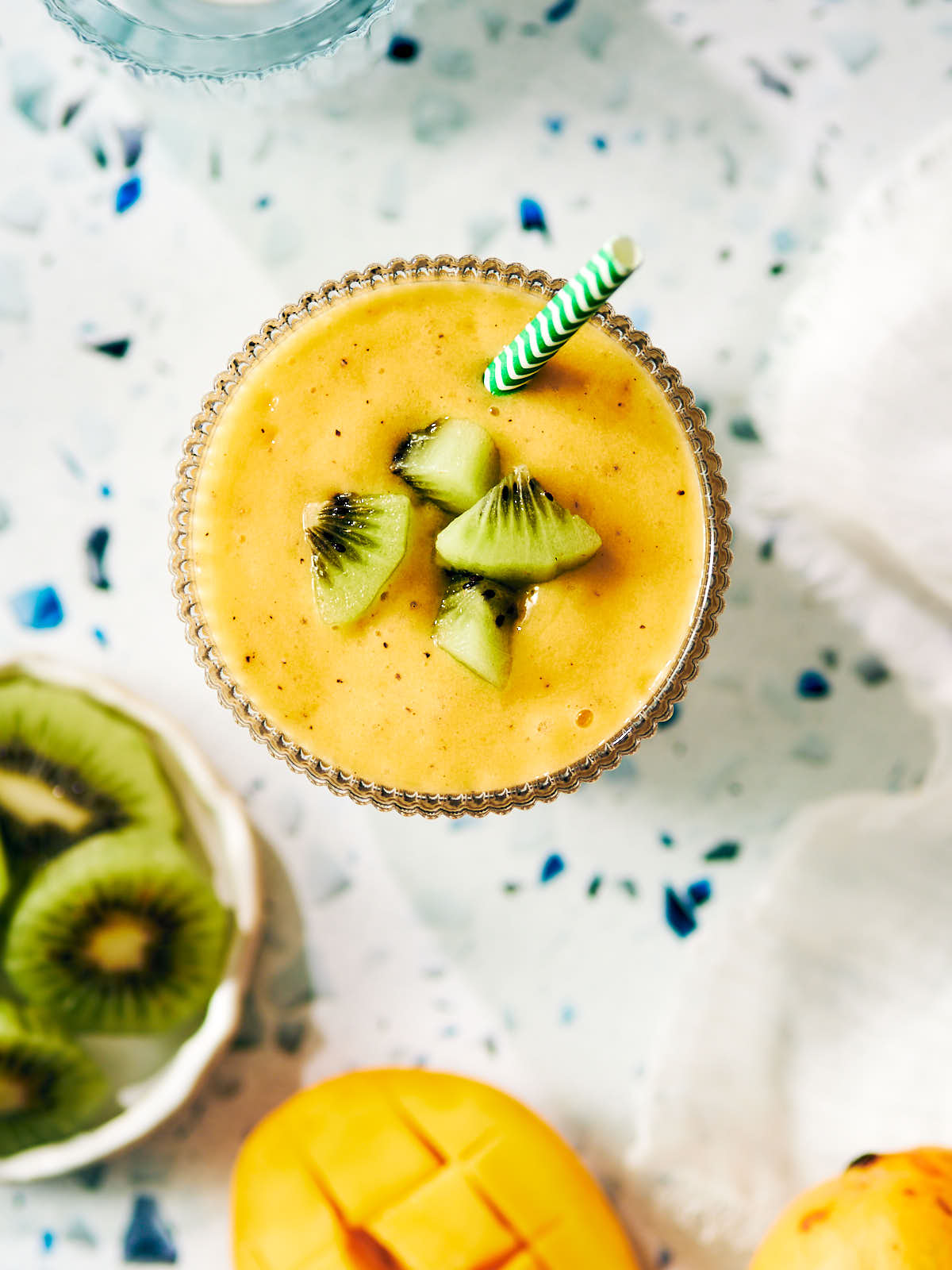Vegan mango smoothie in a glass topped with kiwi and a straw.
