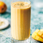 Mango protein smoothie in a glass with hemp seeds sprinkled on top.