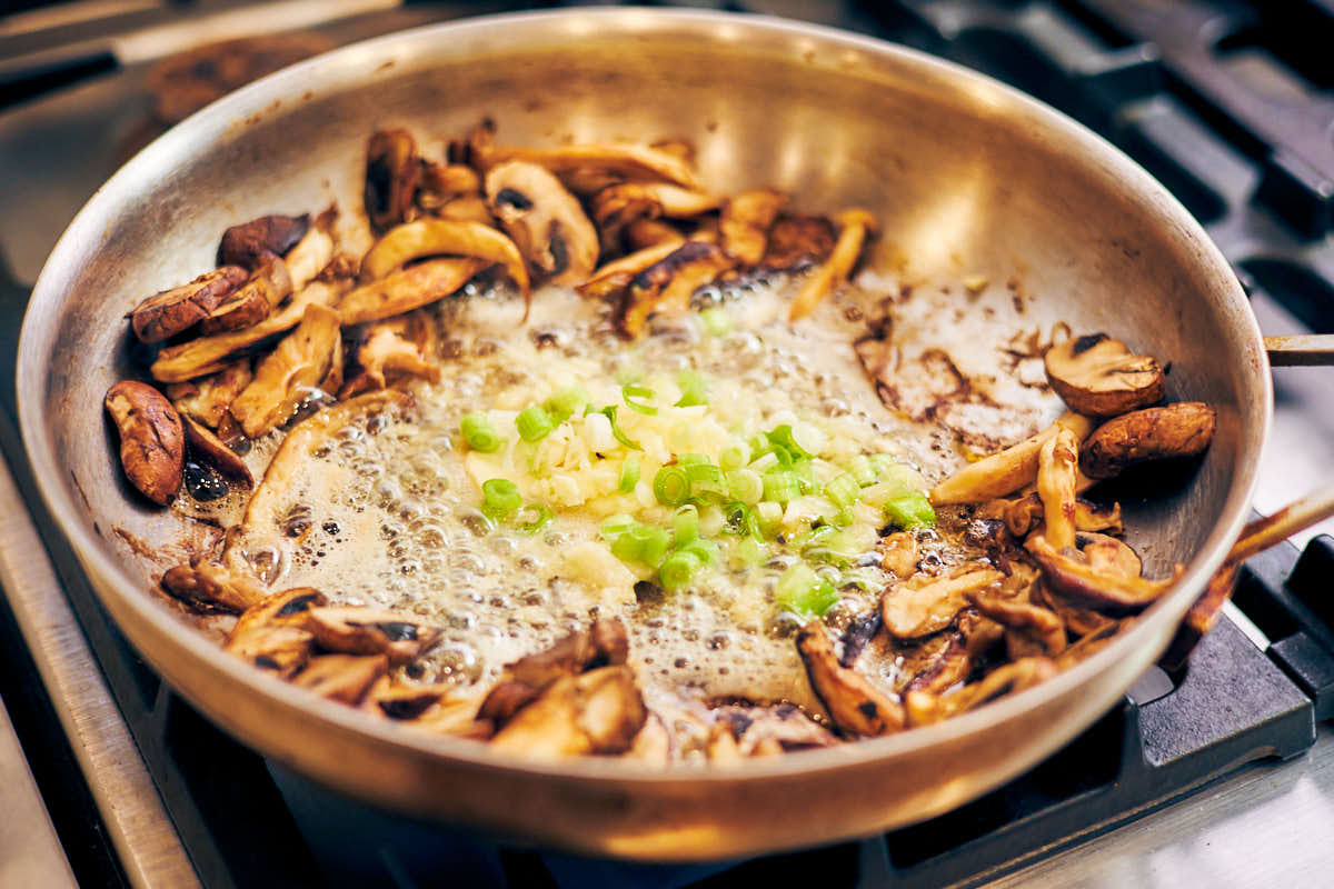 Adding garlic and scallions to melted butter and mushrooms in skillet.