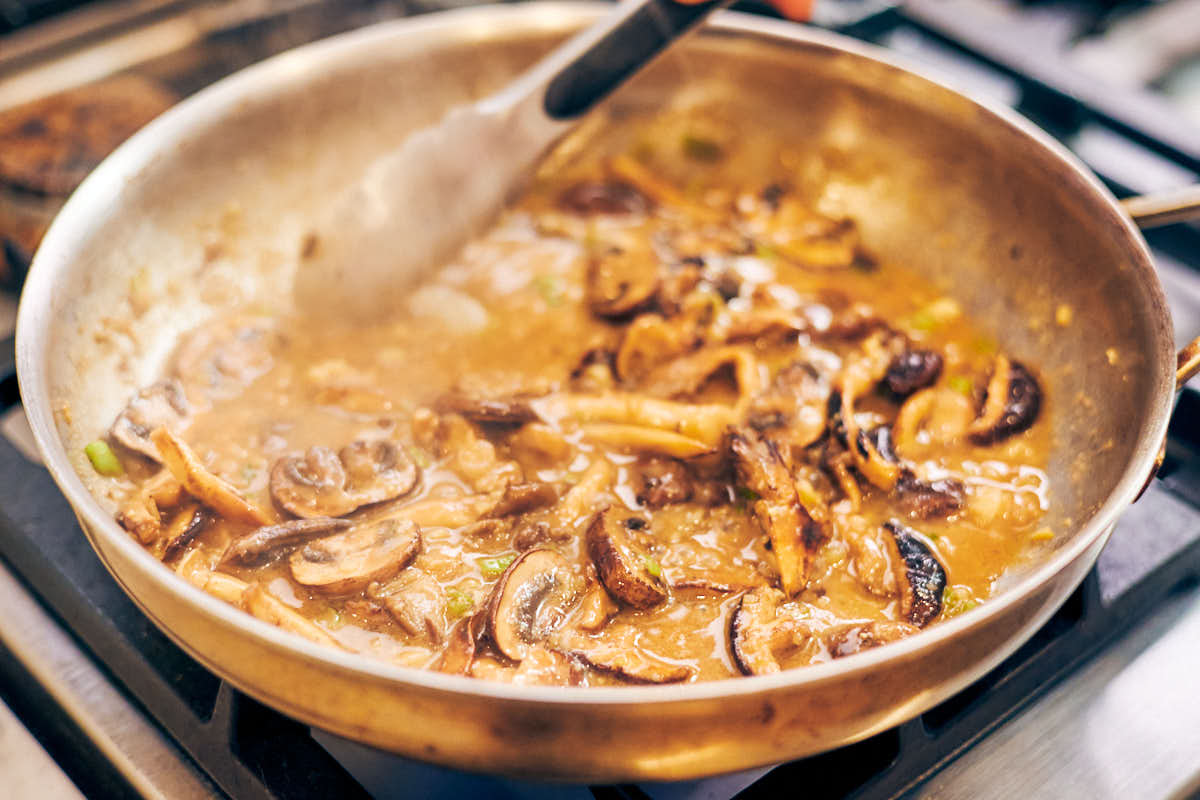 Stirring miso butter sauce in a skillet for mushroom pasta.