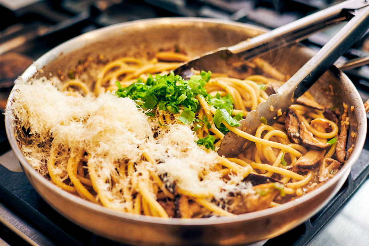Stirring parmesan and green onions (scallions) into mushroom miso pasta.